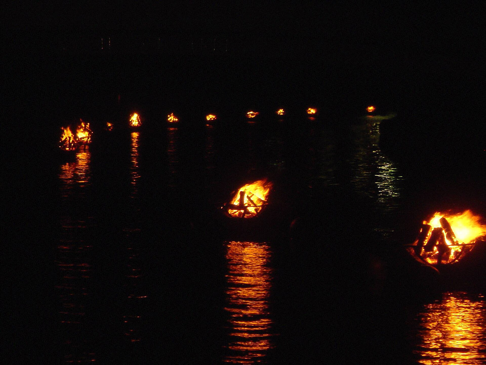 Burning WaterFire braziers reflected in the river at night.