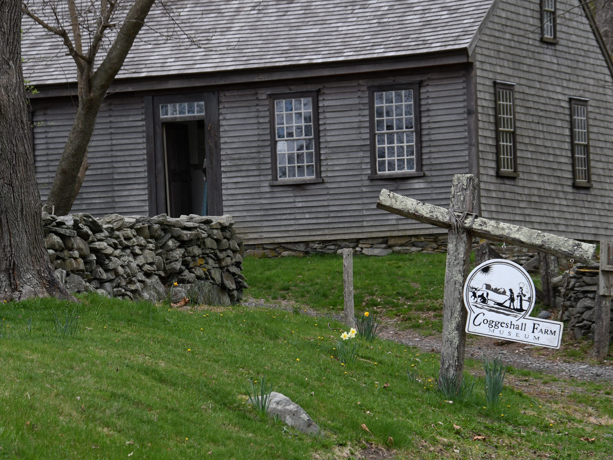 A wooden farmhouse, stone wall and Coggeshall Farm sign.