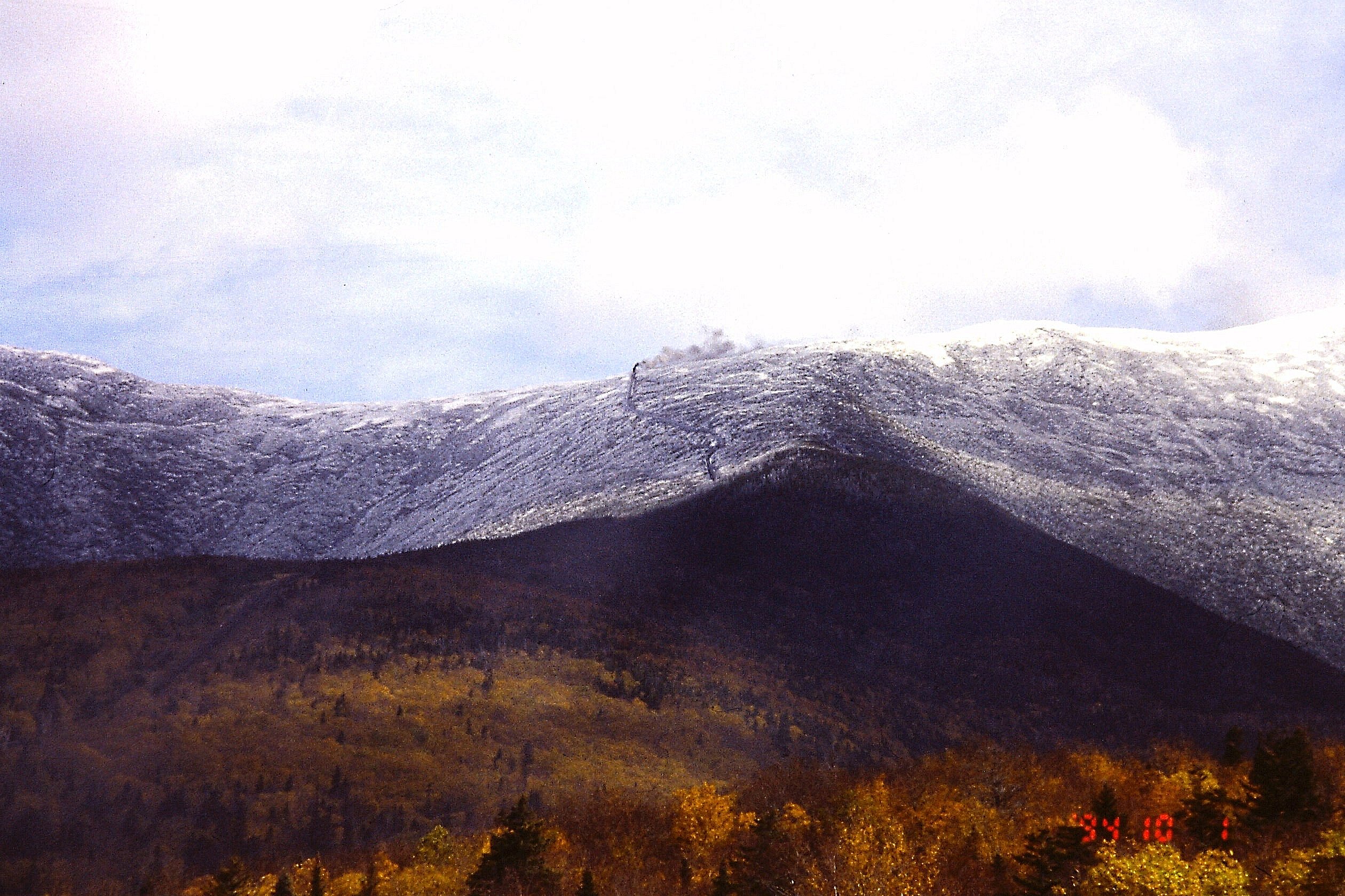 Snow coats the upper slopes of Mount Washington above autumn trees, with the Cog Railway line visible.
