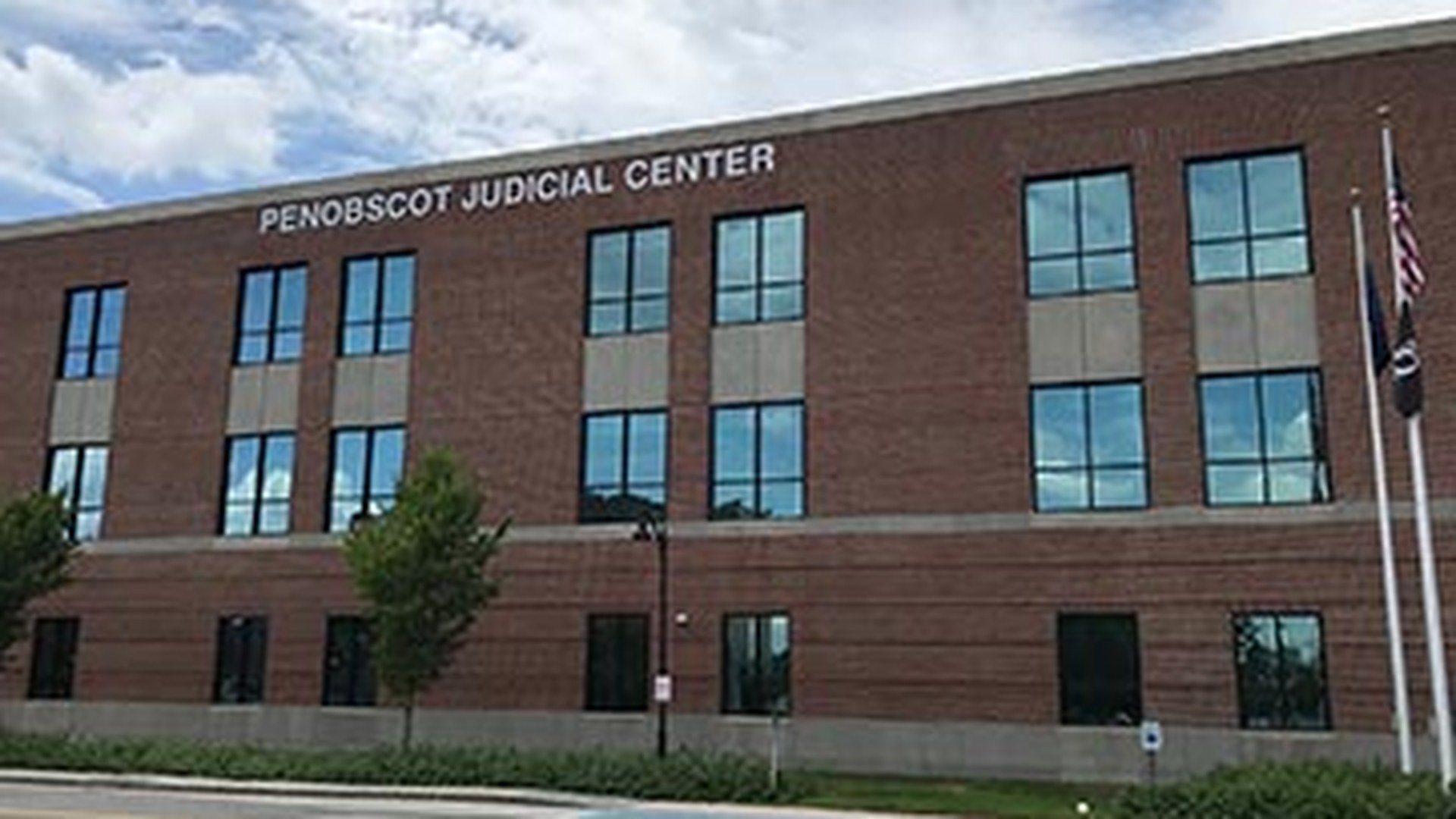 The brick front of the Penobscot Judicial Center, with the name on the building and flags at the right.