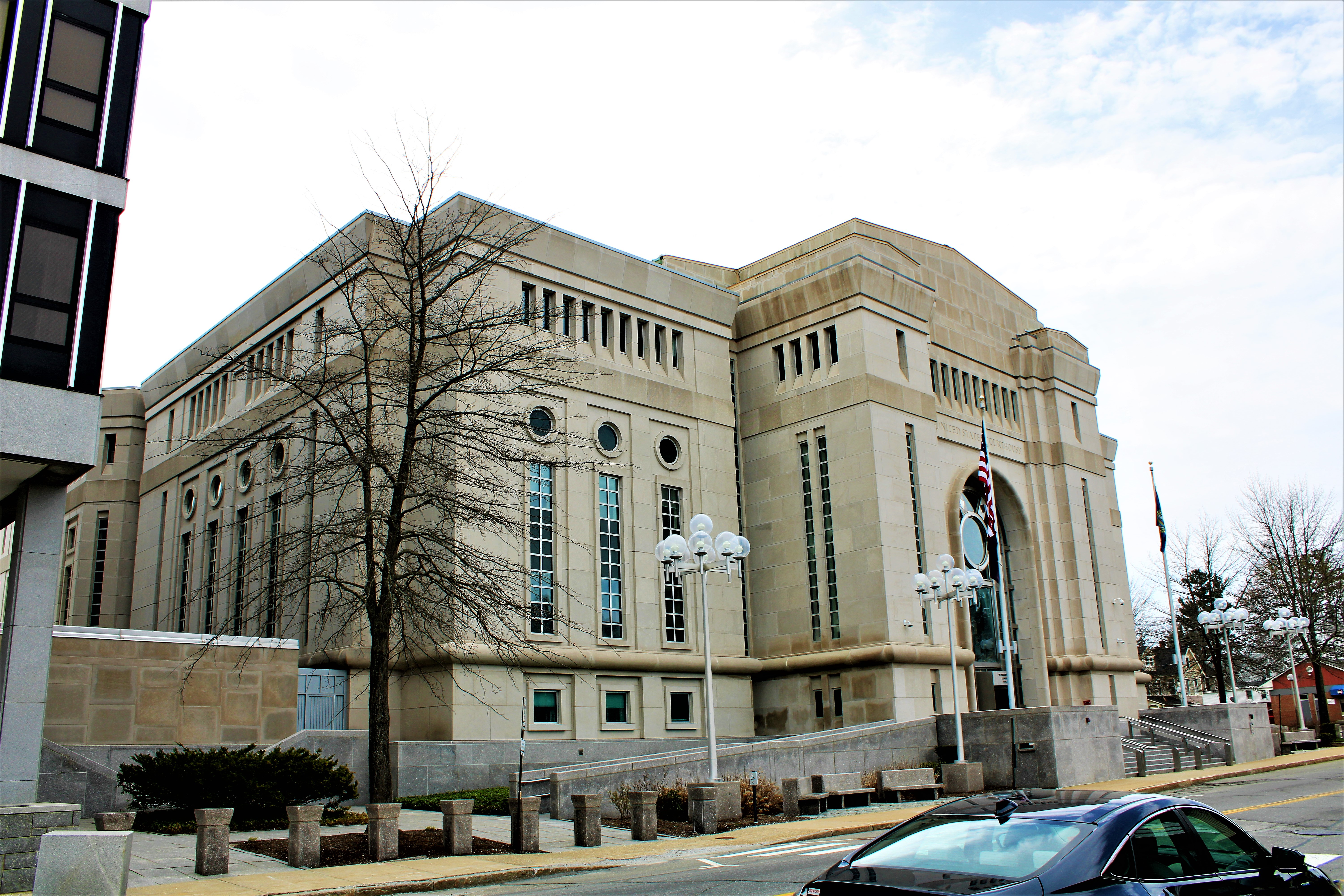 The tan stone Warren B. Rudman U.S. Courthouse in Concord, New Hampshire, with an arched entrance and globe lampposts.
