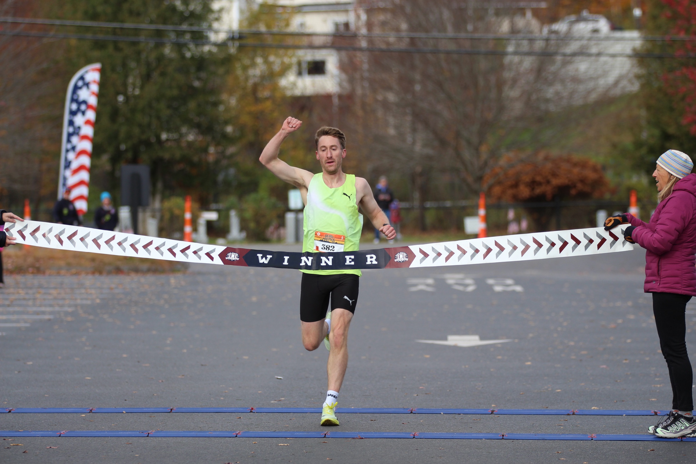 Adam Quinn, wearing bib 382 and a fluorescent yellow-green singlet, raises a fist as he runs through the winner's tape at the Heady Trotter in Stowe.