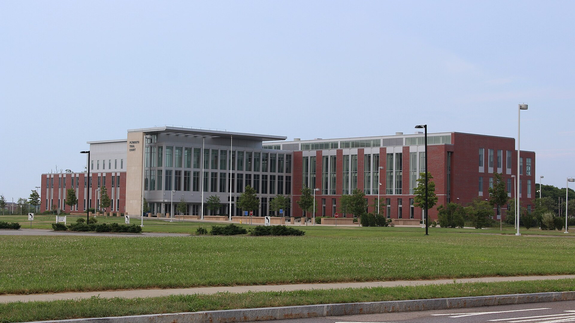 The Plymouth Trial Court, a long brick and glass building with the name on the left tower, seen across a lawn.
